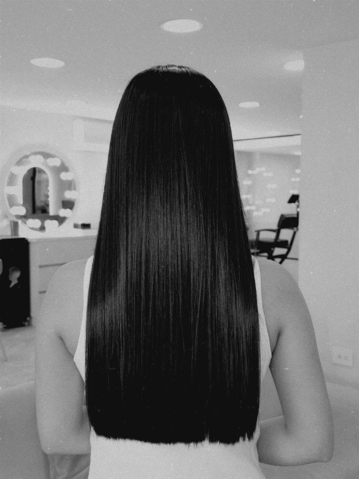 Espalda de una clienta con cabello negro liso hasta la cintura frente a los espejos del salón