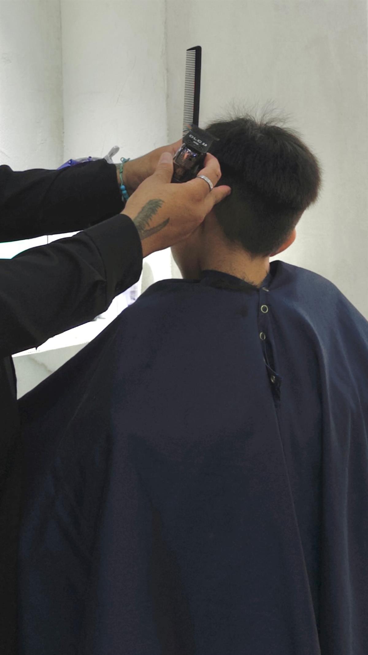Barbero haciendo un corte con máquina a un cliente con capa negra