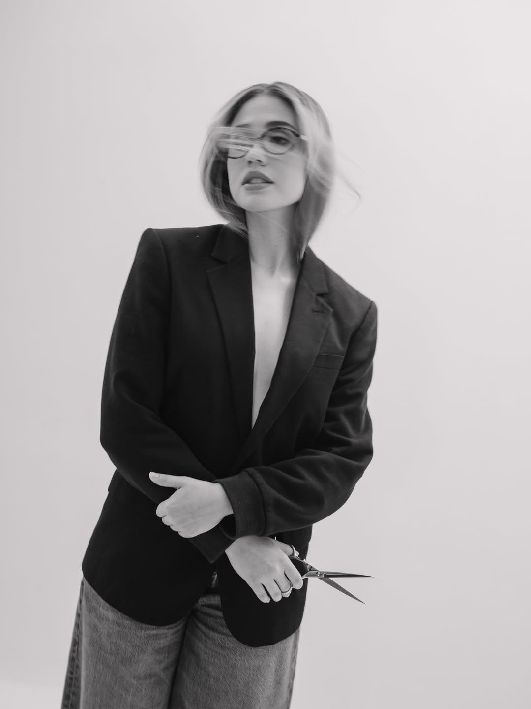 Modelo con blazer negro sosteniendo una tijera