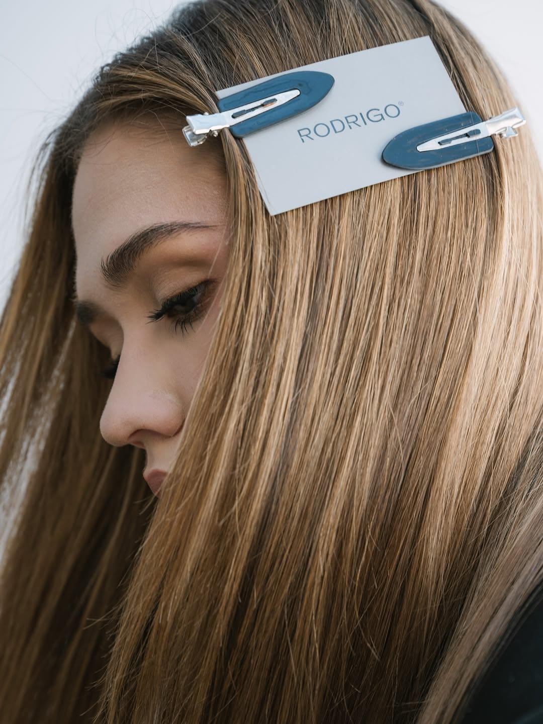 Modelo de perfil con cabello miel liso y dos pinzas azules sobre la tarjeta RODRIGO